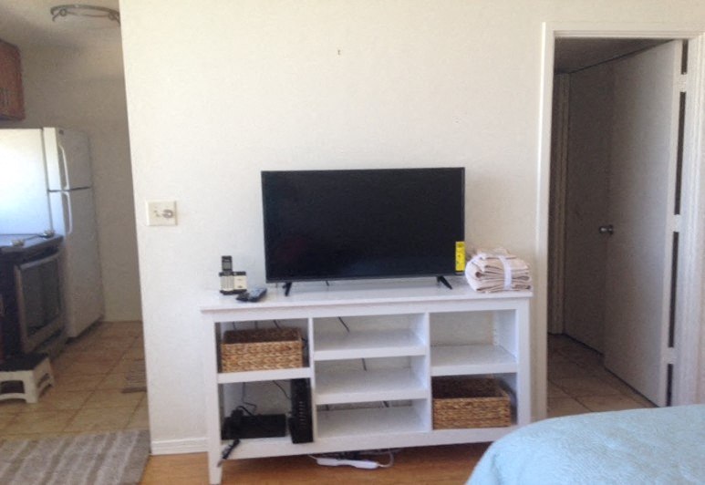 A black television is on a white stand with baskets underneath.